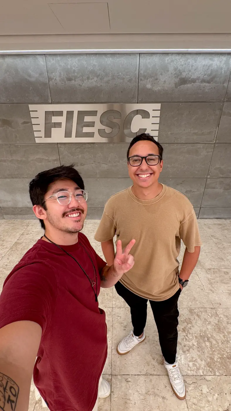 Selfie de Thiago Kai com um colega em frente ao letreiro da FIESC.