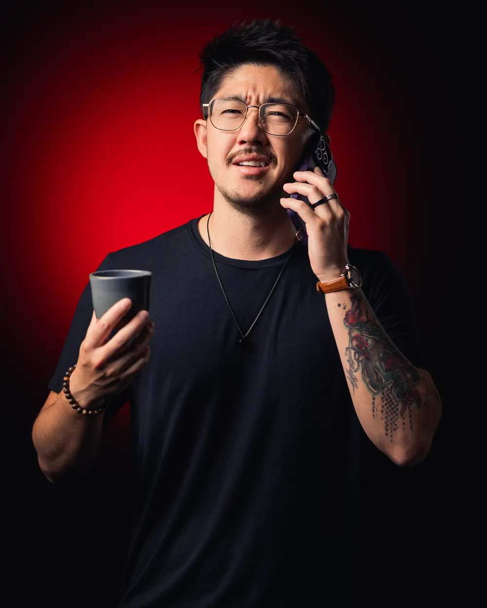 Thiago Kai em fundo vermelho, falando ao celular com um copo de café na mão.